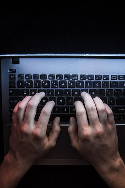 Hands typing on a laptop keyboard in the dark