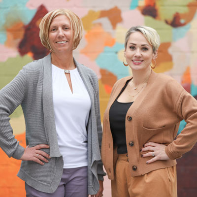 Heather Bowlin and Victoria Bacthel smiling beside a painted mural
