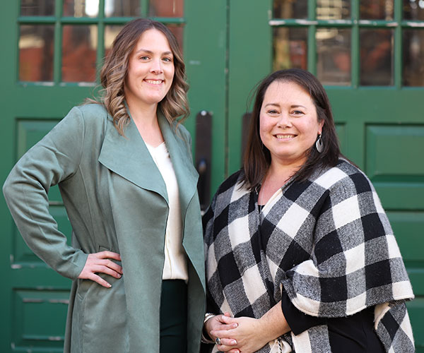Jennifer Spinks and Cortney Shellenberger smiling beside a brick wall