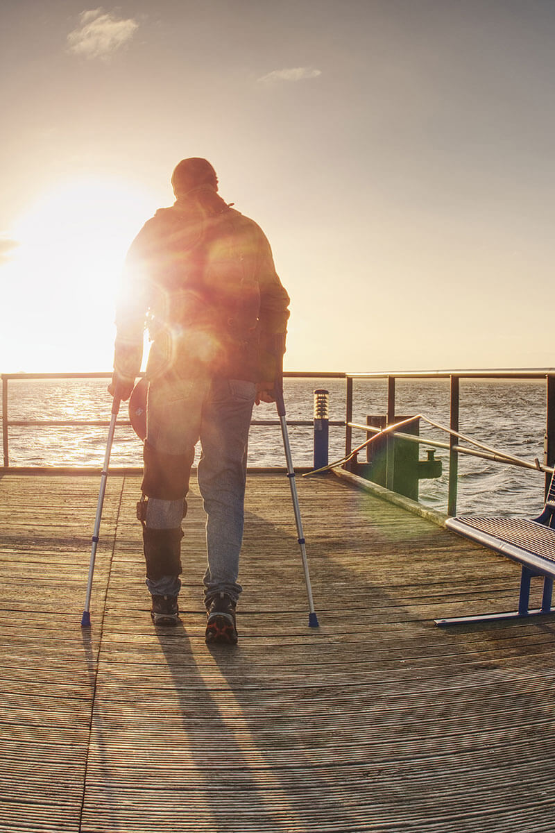 Man using crutches walking on a pier