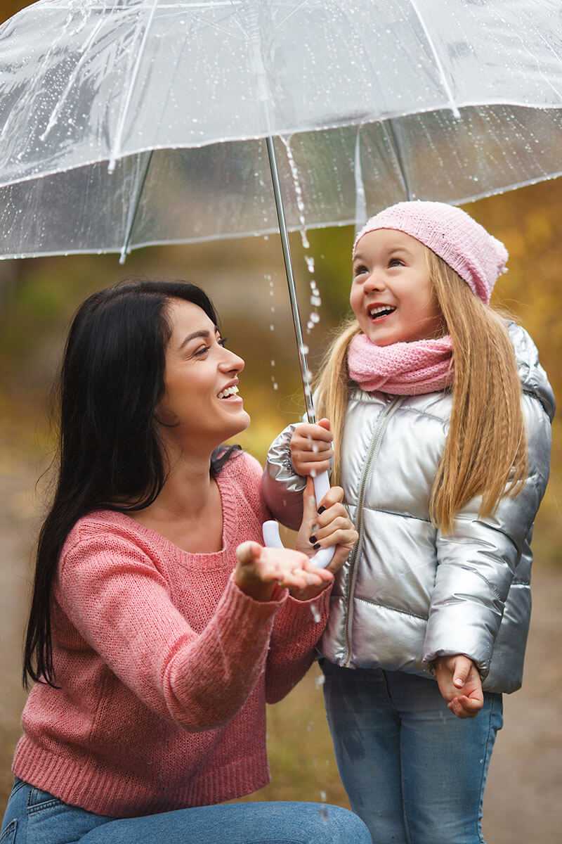 Woman and a child standing under an umbrella while it rains